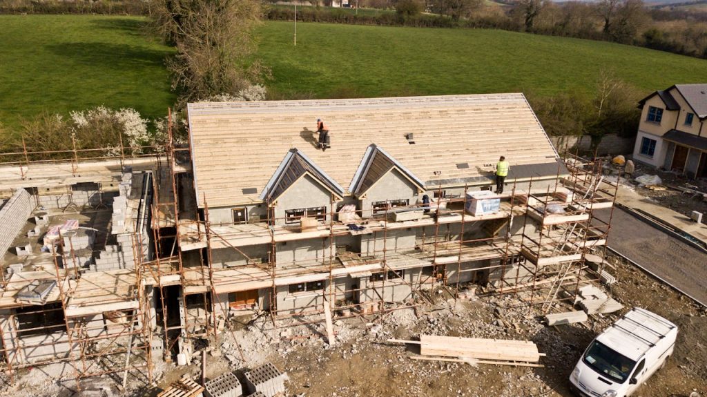 Construction workers on roof of a house under construction with scaffolding surrounded by greenery in rural setting