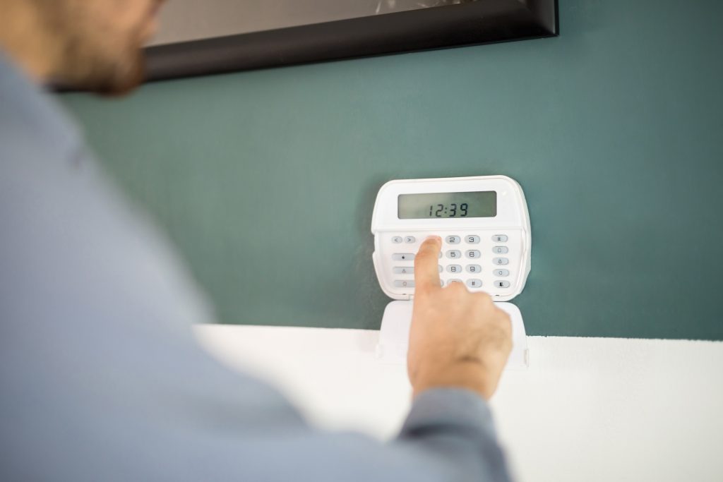 Person pressing buttons on a digital home security alarm keypad mounted on a green wall